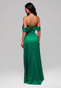 Lange, groene avondjurk van satijn. Heeft off-shoulder mouwen en een getailleerde corsage, die overgaat in een rechte rok. Geen opmerkelijke patronen.