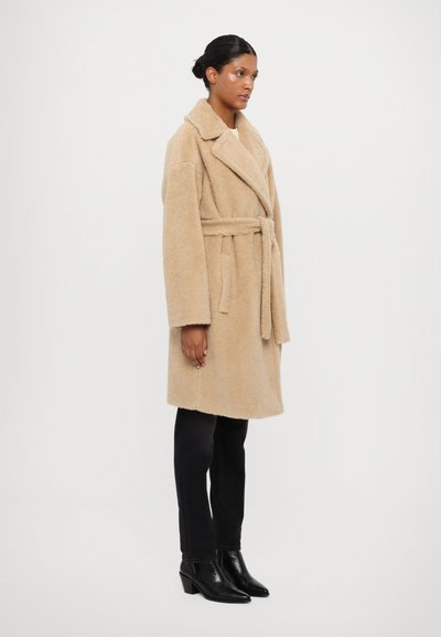 Beige, fluffy wool coat with a wide collar and belted waist; paired with black slim-fit pants and pointed ankle boots.