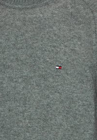 Grauer Strickpullover mit Rundhalsausschnitt und kleinem, gesticktem Logo in Rot, Weiß und Blau im linken Brustbereich.