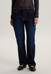 Jeans in denim blu scuro con cuciture a contrasto, design a gamba dritta, stile cinque tasche e leggero scolorimento sulle gambe.