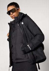 Zwarte waterdichte jas met een gevoerd interieur, voorzien van een hoge kraag, ritszakken en een GORE-TEX-logo op de mouw.