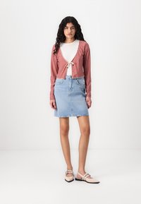 Rød og hvit rute mønster cropped cardigan med knytning foran, sammen med et lys blå denim blyantskjørt. Modellen har på seg beige flate sko.