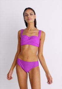 Lila bikini texturált, keresztezett felsőrésszel és széles pántokkal; hozzá illő, magas derekú alsókkal. Sima, rugalmas anyag, testhezálló fazon.