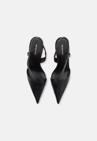 Talons hauts slingback en cuir noir avec un bout pointu, dotés de lanières croisées et d'une fermeture à boucle métallique. Logo en relief sur la semelle intérieure.