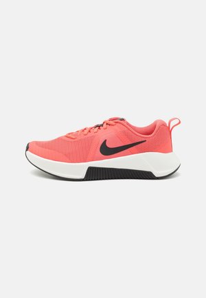 Zapatilla Nike color coral rosa con logo swoosh negro, media suela blanca, suela externa negra, parte superior de malla, cordones y lengüeta en el talón sobre fondo blanco.