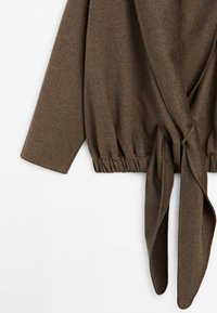 Brown wrap-style sweater with long sleeves and gathered elastic waistband, tied in a loose knot at the front bottom.