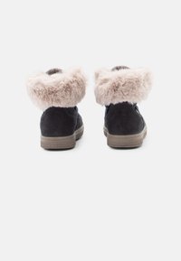 Bottines bleu foncé avec un col en fausse fourrure beige doux. Elles disposent d'une semelle en caoutchouc texturé et d'un matériau en daim lisse.