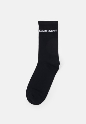 Černé žebrované ponožky s bílým logem "CARHARTT" na vrchu. Měkký, elastický materiál s klasickým sportovním designem.