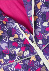 Lila Windbreaker mit einem Herzmuster in verschiedenen Farben. Innenfutter in Pink, mit einem auffälligen weißen Reißverschluss und Nähte.