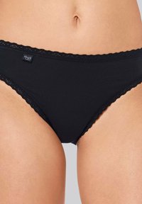 Schwarze Baumwollslips mit zarter Spitze am Bund und an den Beinen, mit einem kleinen Markenlabel vorne. Weicher Stoff.