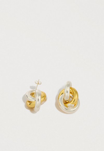 Σκουλαρίκια κόμπου σε χρυσό και ασήμι με γυαλιστερό φινίρισμα· το ένα σκουλαρίκι έχει μια μονή διαμαντένια πινελιά στο μεγαλύτερο μέρος.