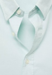 Vaaleansininen kauluspaita, jossa on napitettava etuosa, jossa on kaksi valkoista muovipainiketta ja sileä, teksturoitu kangas.