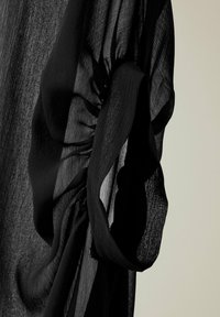 Czarna przezroczysta tkanina o zebranym i skręconym wzorze na jasnym tle, podkreślająca przezroczystość i delikatny splot materiału.