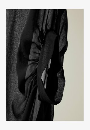 Tissu noir transparent avec une texture froncée et torsadée sur un fond clair, mettant en valeur la transparence et le tissage fin du tissu.