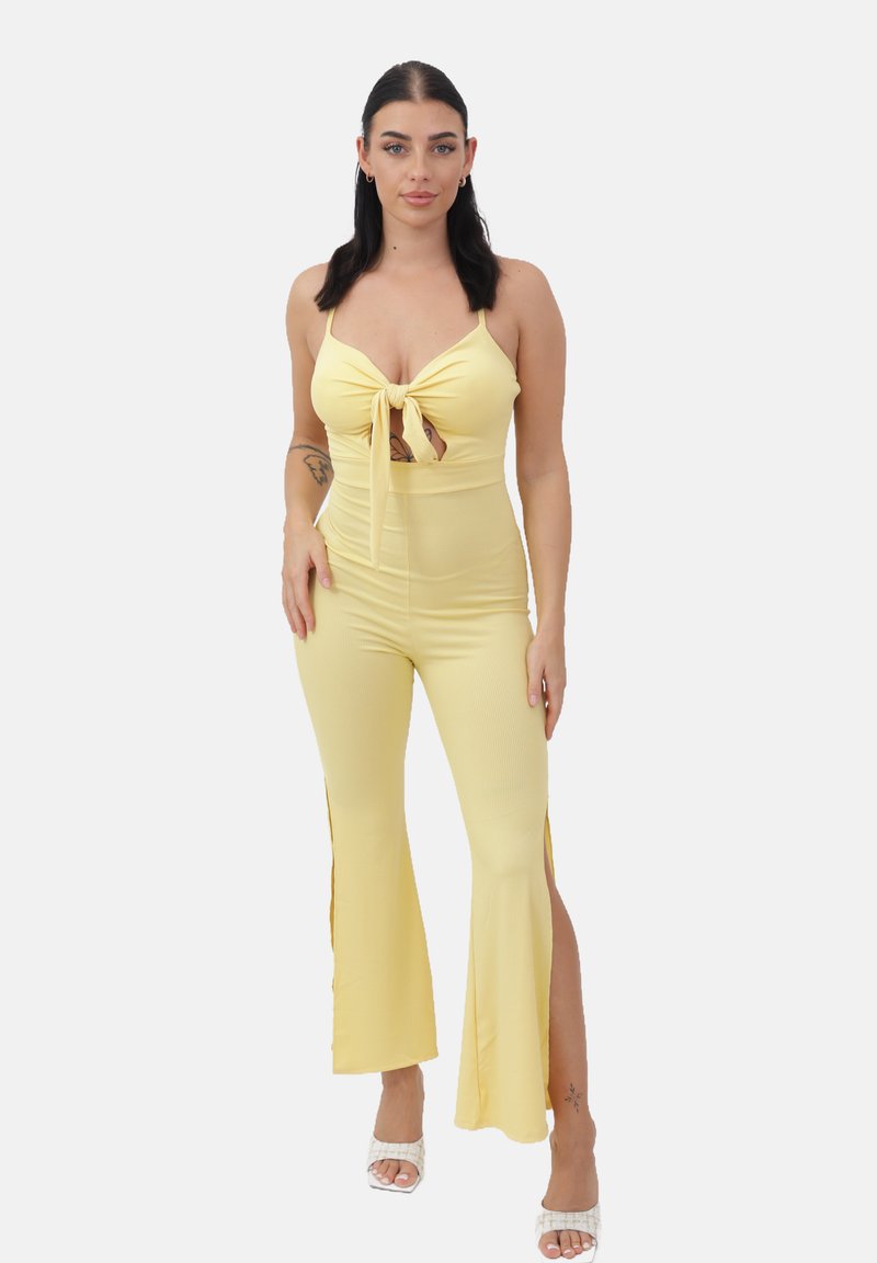 Mono amarillo con detalle de nudo en la parte delantera, ajustado con piernas acampanadas y aberturas laterales. La textura acanalada realza el interés visual.