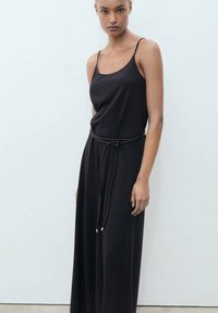 Vestido negro sin mangas con un corte relajado, presenta un cinturón trenzado en la cintura y una textura suave y lisa.