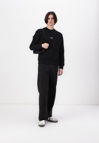 Black sweatshirt with logo, long sleeves, ribbed cuffs, paired with loose black denim pants and grey and white sneakers. Black shoulder bag.