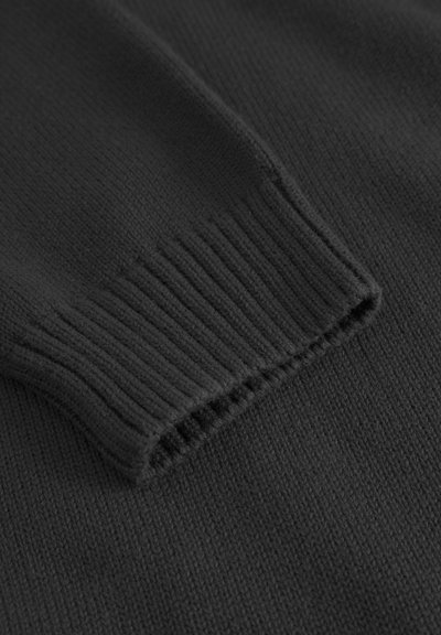 Tejido de suéter negro de punto con puños ribeteados. Textura suave con un ligero estiramiento. El borde del puño está terminado con costuras cuidadosas.