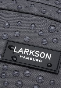 Gråt stof med en tekstureret overflade, der har vanddråber. En sort etiket med hvid tekst lyder "LARKSON HAMBURG."