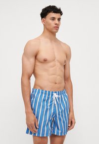 Blue striped swim shorts with an elastic waistband and white drawstring. Features vertical light orange stripes and a smooth, lightweight texture.