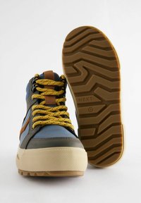 Wysokie sneakersy w kolorystyce niebiesko-brązowo-szarej, z teksturowaną gumową podeszwą oraz kontrastującymi żółtymi sznurowadłami z czarnymi drobinkami.