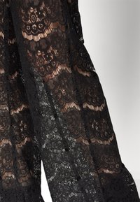 Zwarte kantstof met bloemmotieven, met een doorschijnende textuur. Het ontwerp bevat gelaagde secties, wat diepte en visuele interesse toevoegt.