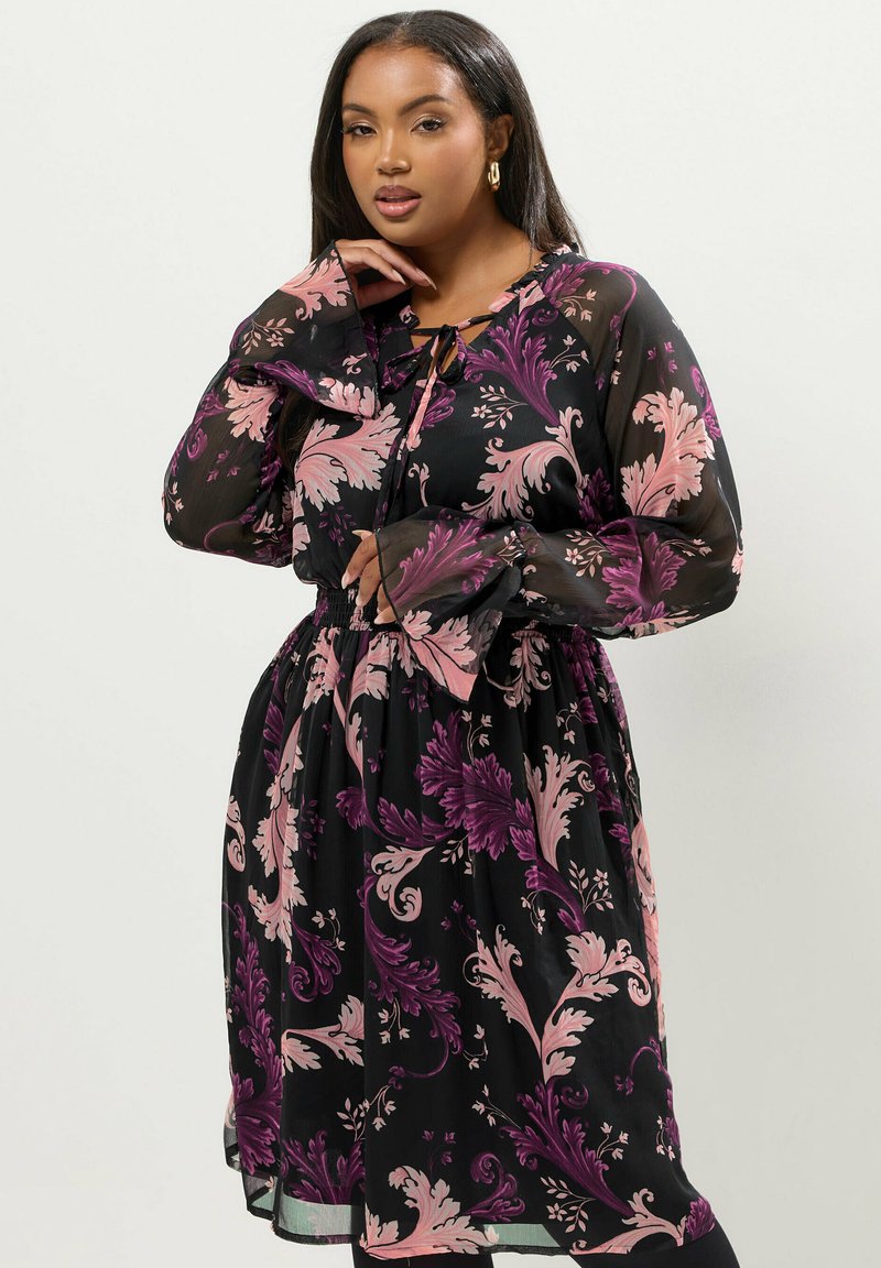 Svart genomskinlig klänning med rosa och lila blommönster, långa ärmar, nyckelhalsringning och elastisk midja. Mjuk textur och svävande design.
