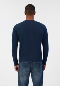 Chemise à manches longues bleu marine avec un col rond, en tissu lisse. Associée à un jean en denim délavé présentant des poches et un style décontracté.