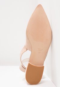 Chaussure beige en daim à bout pointu avec bride arrière, montrant une semelle texturée et taille 37 marquée "Made in Spain."