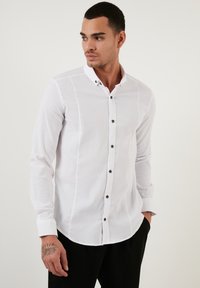 Hvid langærmet skjorte med tekstureret finish, med krave med knaplukning og mørke knapper langs fronten, tætsiddende design.