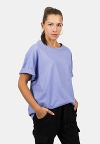 Relaxed-fit lavender cotton T-shirt with rolled sleeves and a crew neckline, paired with black pants, showcasing a smooth texture.
