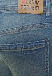 Plave traperice prikazuju detaljan pogled na stražnji dio s kožnom oznakom označenom "DENIM PROJECT" i vidljivim detaljima šivanja.