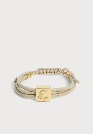 Bracelet beige en cordon et cuir avec un pendentif carré doré gravé d’un C, doté d’un nœud ajustable et de fermoirs dorés.