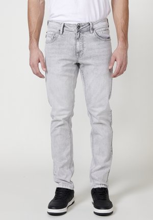 Vaqueros de denim de color gris claro con un corte ajustado. Incluyen cinco bolsillos, un cierre de botón y un leve desgastado para dar textura. Combinados con zapatillas negras.