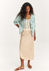 Svetlomodrá džínová bunda cez krémový pletený top, spárovaná s béžovou maxi sukňou s kvetinovým vzorom a hnedými sandálmi. Neutrálna farebná paleta.