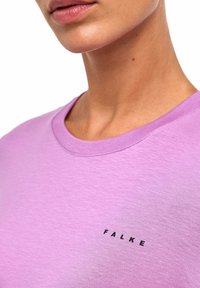 Hellviolettes T-Shirt mit Rundhalsausschnitt aus weichem Stoff, mit kleinem schwarzem "FALKE"-Logo im Brustbereich und glatter Textur.