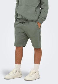 Lys grønne shorts i bomuldsblanding med elastisk talje, sidelommer og en afslappet pasform, parret med hvide sneakers og ankelsokker.