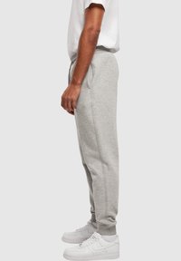 Gray sweatpants made of cotton blend fabric, featuring a drawstring waistband, elastic ankle cuffs, and side pockets. Paired with white sneakers.