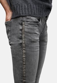 Vaqueros de mezclilla gris de corte slim, con un acento texturizado de estampado de leopardo a lo largo de la costura lateral y bolsillos tradicionales.