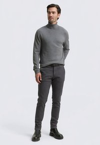 Grauer Rollkragenpullover kombiniert mit dunkelgrauen, schmal geschnittenen Hosen und schwarzen Stiefeletten. Glatter Stoff, figurbetontes Design, keine sichtbaren Muster.