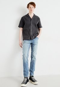 Camisa de manga corta gris oscuro con botón frontal, combinada con jeans azul claro y zapatillas negras de caña alta. Tejido suave y corte holgado.