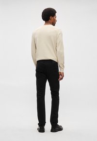 Ανοιχτό μπεζ πουλόβερ με υφή, συνδυασμένο με μαύρο στενό παντελόνι. Το σύνολο ολοκληρώνεται με μαύρα, παπούτσια με χοντρή σόλα.