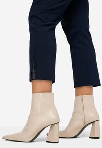 Beige Stiefeletten mit spitz zulaufender Zehe, glatter Lederstruktur und geometrischem Blockabsatz. Mit einem seitlichen Reißverschluss zum Verschließen.