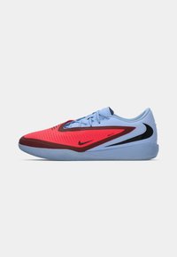 Nike sports shoe featuring a blue upper, red accents, a textured design, and a black logo. Rubber outsole with a patterned grip.