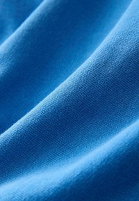 Gros plan d'un tissu bleu lisse avec une texture tricot visible et des plis doux créant des ombres légères.