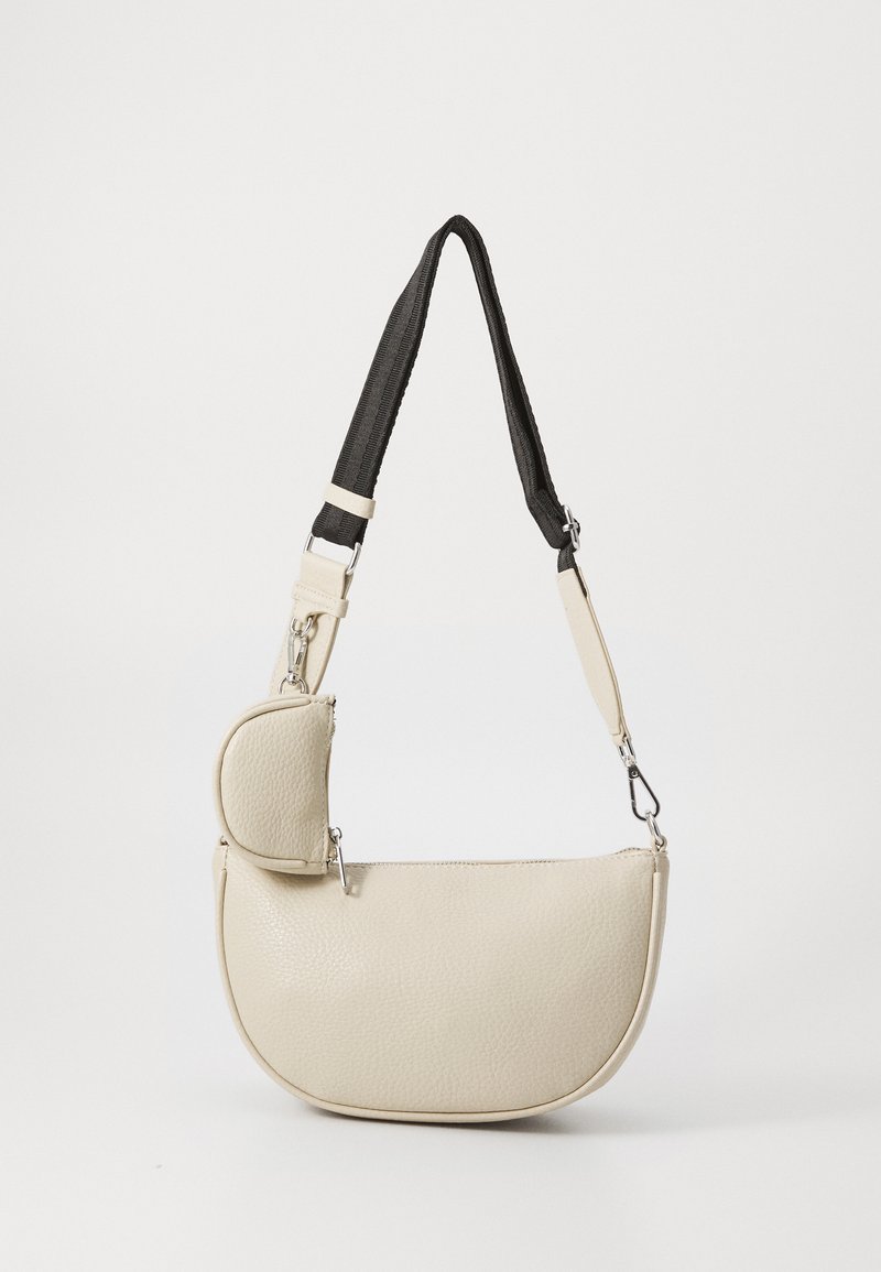 Beige leather shoulder bag with a textured finish, curved shape, and a small zippered compartment. Features a black adjustable strap.