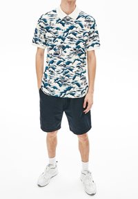 Pikapaita, jossa on sinivalkoinen aaltoaihe ja valkoinen kontrastikaulus. Yhdistetty tummiin raidallisiin shortseihin ja valkoisiin lenkkareihin.