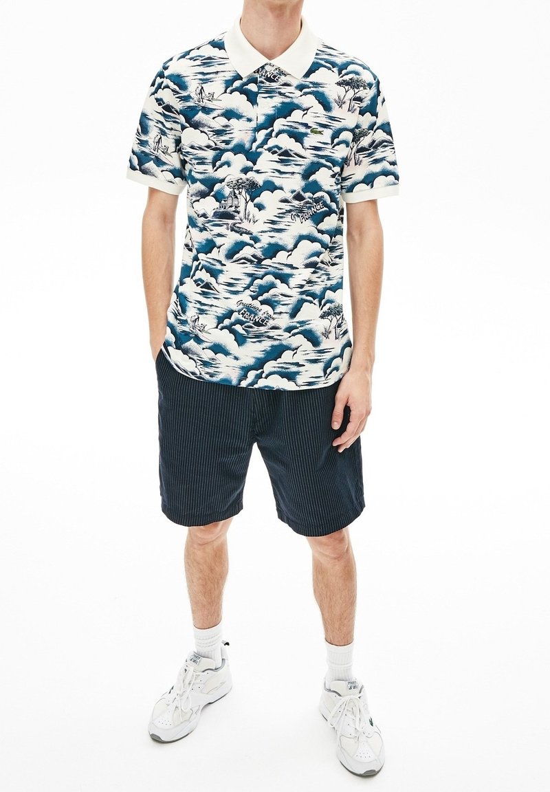 Pikapaita, jossa on sinivalkoinen aaltoaihe ja valkoinen kontrastikaulus. Yhdistetty tummiin raidallisiin shortseihin ja valkoisiin lenkkareihin.