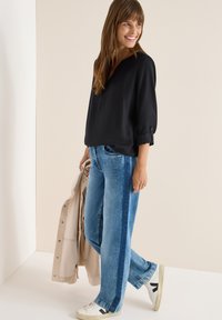 Sort bluse med korte ærmer har en lav V-udskæring; parret med lysblå brede jeans med side-striber. Hvide sneakers fuldender looket.