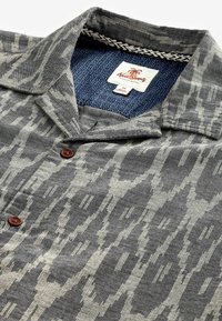 Grijze short-sleeve shirt met een gestructureerd patroon; voorzien van bruine knopen, een kraag en een contrasterende blauw gepatterde binnenkant.